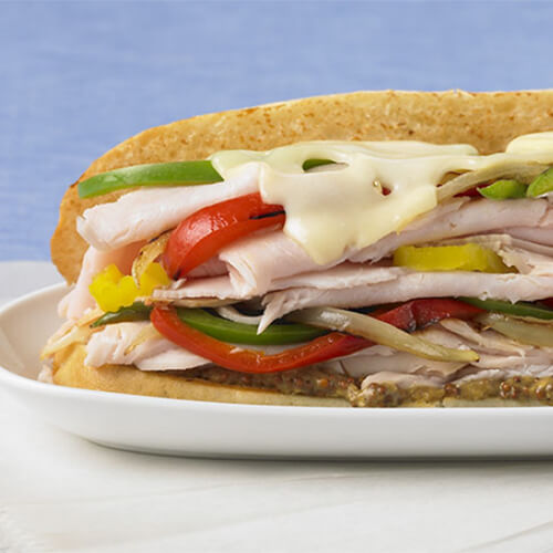 Deli-sliced turkey meat with pickles, red and green pepper, whole-grain mustard and Swiss cheese on a hoagie.