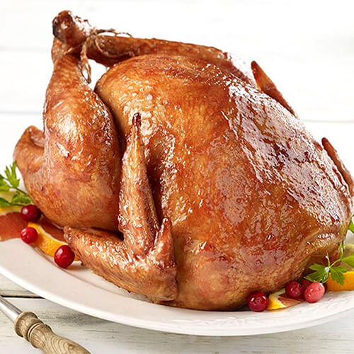 A whole turkey covered with a cranberry glaze, atop a variety of berries and fruits, atop a white plate.