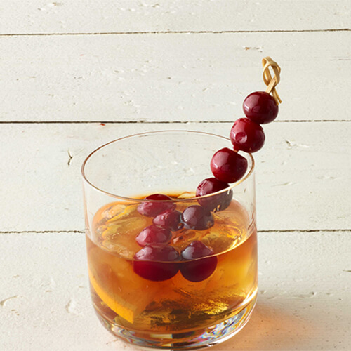 Cranberry old fashioned garnished with cranberries on a white wood table.