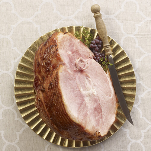Cranberry orange glazed ham on a striped plate on a beige patterned tablecloth.