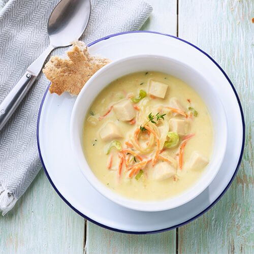 Creamy dijon turkey soup in a white bowl on a white plate with a side piece of bread.