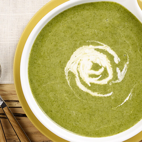 A creamy spinach soup served in a green bowl on a linen tablecloth.