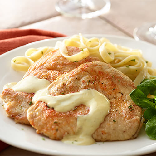 Creamy turkey cutlets served with pasta and spinach, served in a white bowl on a wooden table.