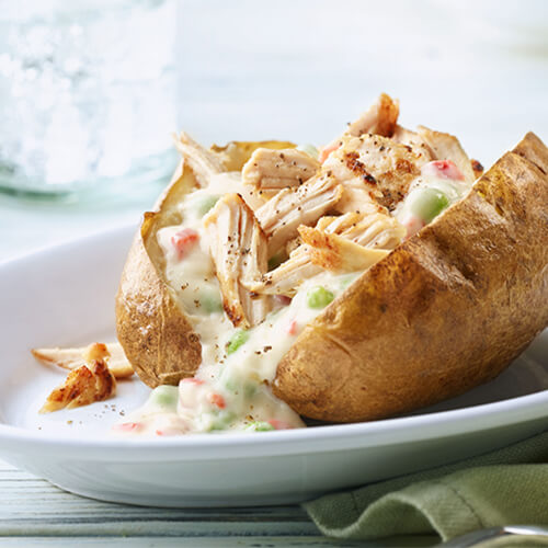 A creamy sauce, turkey breast tenderloins, butter and peas, covering a baked potato, served on a white plate.