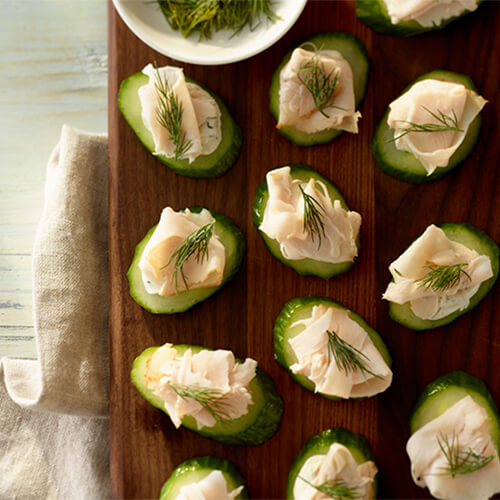 Cucumber turkey bites garnished with a sprig of dill on a wood plank.