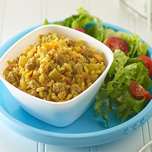 Brown rice, packed with veggies and turkey breast served in a white bowl with a side of salad on a blue plate.