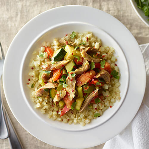 Curry-sauteed veggies, made with cauliflower crumbles and turkey, served on a large white plate.