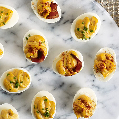 Deviled eggs with bacon sitting on a white marble plate.