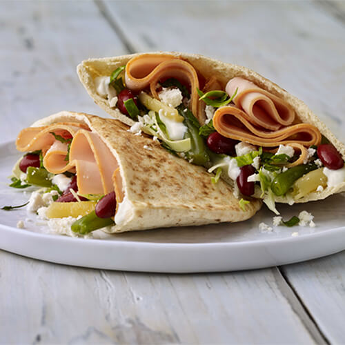 Greek turkey pitas overflowing with filling on a white plate on a wood table.