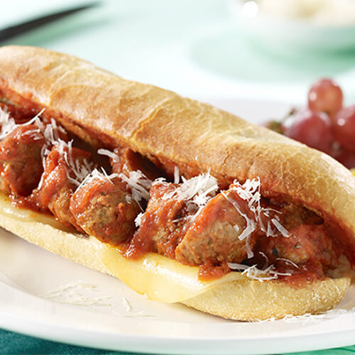 A hearty amount of turkey meatballs, parmesan and Provolone cheeses, swimming with pasta sauce, served on a hoagie bun on a white plate, garnished with orange slices and grapes.
