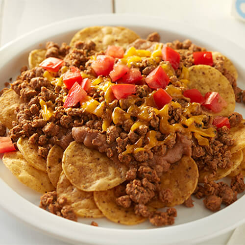 Layered tortilla chips, refried beans and turkey, topped with cheese and tomatoes and served on a white plate.