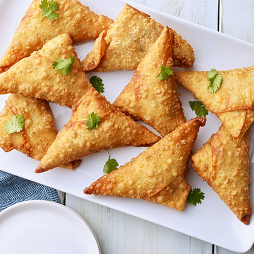 Turkey samosas garnished with cilantro stacked on a white plate.