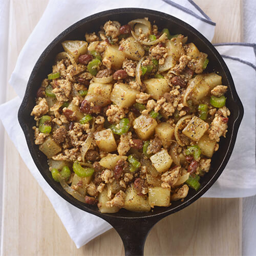 A hearty amount of lean ground turkey, potatoes, and a healthy amount of vegetables in a black skillet, on a wooden cooking tray.