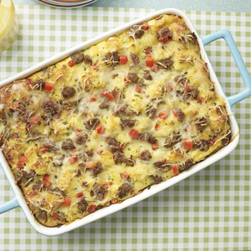 A comforting bake made from French bread, cheese, egg, peppers and turkey, served in a blue baking dish atop a green checkered table mat.