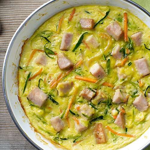 A hearty frittata, chock full of veggies and deli turkey, served in a painted bowl, on a linen placemat.