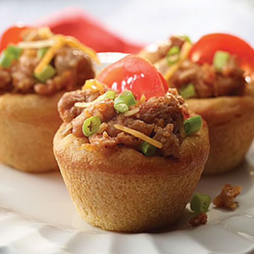 3 taco cups topped with taco seasoned JENNIE-O® ground turkey, green onion, tomato, and Mexican cheese on a white plate.