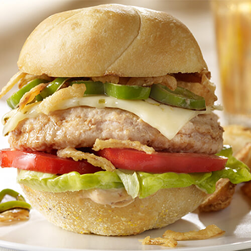 A lean turkey burger filled with grilled jalapeno slices, fresh chipotle adobo sauce, and jalapeno jack, served with lettuce and tomato, with a side of potato wedges on a white plate.