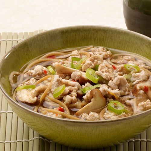 Peppery noodle bowls filled with lean turkey and sautéed vegetables, garnished with green onions, served in a green bowl with chopsticks on a green bamboo placemat.