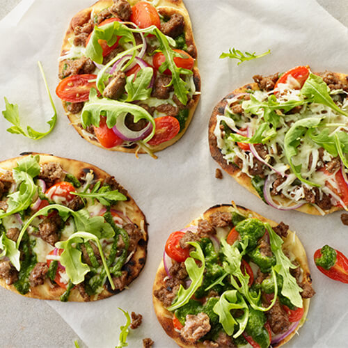 Flatbread turkey sausage pizza with the toppings overflowing on a white table.