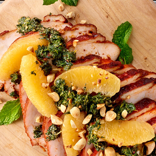 Orange and mint smoked turkey garnished with fresh mint on a wood board.