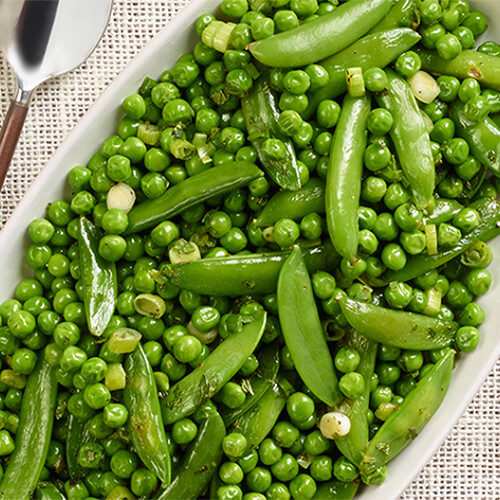 A hearty about of peas and green onion with mint sirred in and seasoned, served on a white platter atop a linen tablecloth.