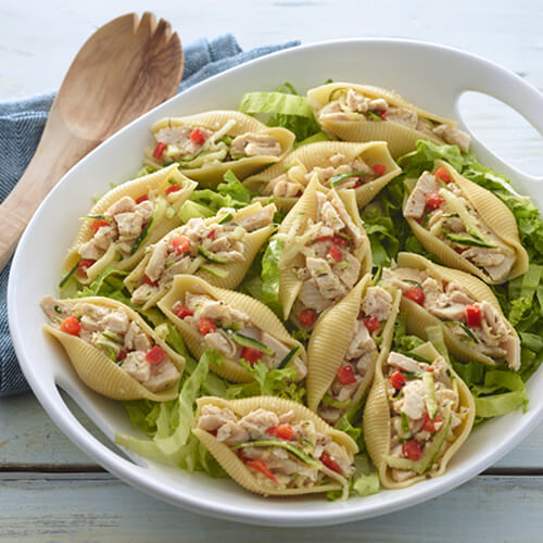 Garden turkey salad in shells on a bed of lettuce in a white bowl on a white table.