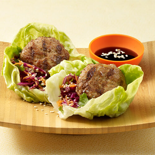 Lettuce wraps packed with fresh veggies, small turkey patties and topped with toasted sesame seeds, served with soy sauce on a wooden plate.