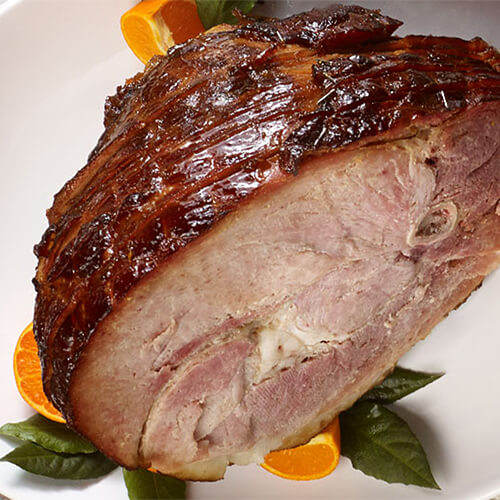 Glazed cure cherrywood smoked ham garnished with orange on a white plate.