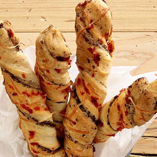 Incredible breadsticks feature roasted red pepper, olive spread and Parmesan cheese, served in a small pail lined with baking paper on a wooden table.