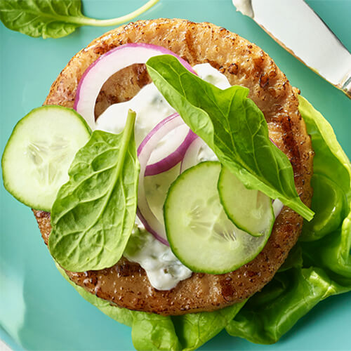 Vegetables on turkey patty garnished with basil on a blue plate.