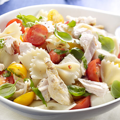 A salad packed full of fresh veggies, bowtie pasta, and slow-cooked turkey, served on in a white bowl.