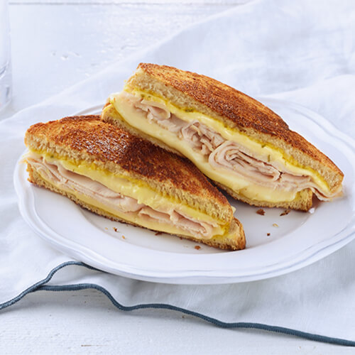 Layers of melted cheese, oven roasted deli turkey and flavorful mustard spread atop sourdough bread on a white plate and table.