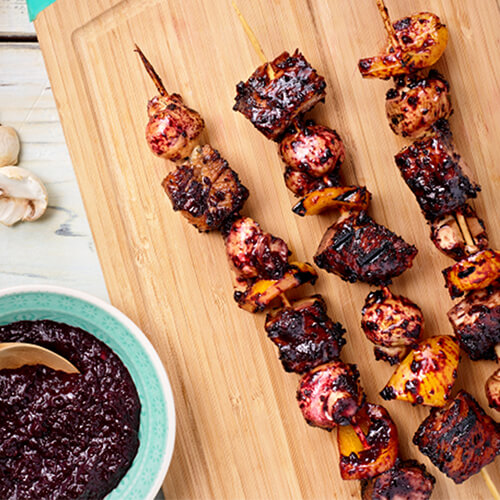 Grilled turkey kabobs with cherry chipotle sauce on a wood cutting board.