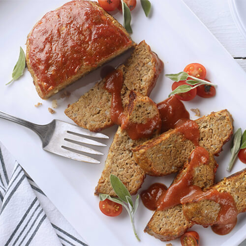 Grilled turkey meatloaf with cherry tomatoes sliced on a white plate.