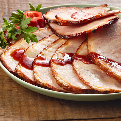 Ham with sriracha glaze garnished with cilantro on a grey plate on a wood table.