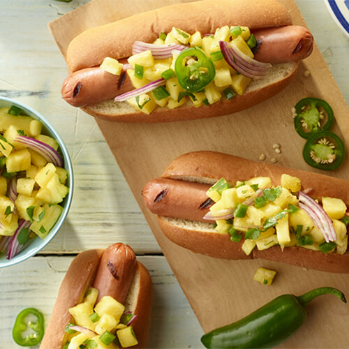 Hawaiian turkey hot dogs garnished with jalapeno on a wood plate.