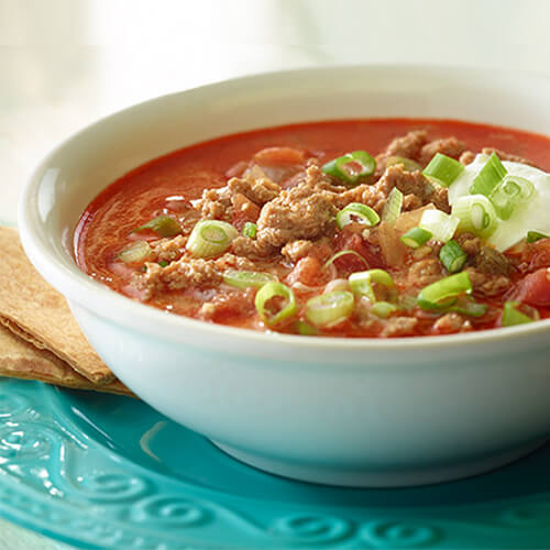 A hearty soup filled with ground turkey, onions, sour cream and crunchy tortillas, served in a white bowl atop a blue plate.