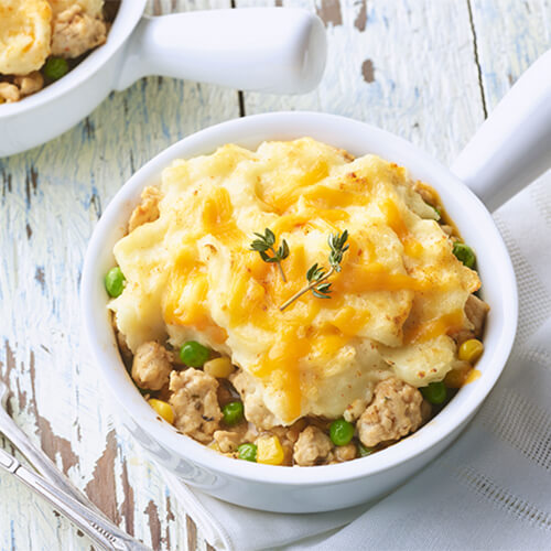 Savory ground turkey, mashed potatoes and cheese, chock full of vegetables, in a soup bowl atop a wooden table.