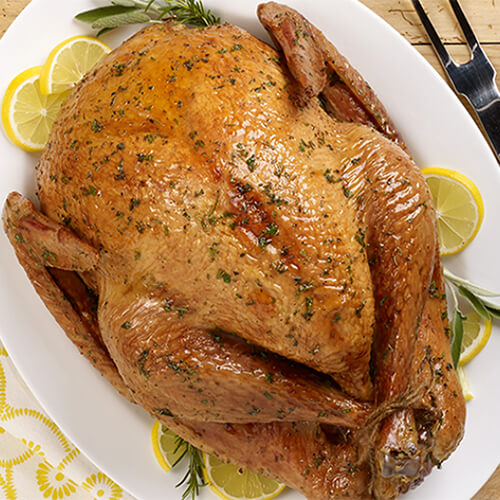 A juicy honey glazed turkey garnished with lemon slices and herbs, served on a white plate atop a wooden table.