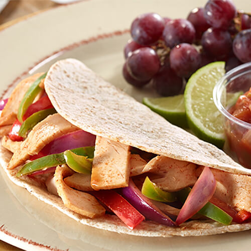 A tortilla filled with bell peppers, turkey, and onion, served with a chili sauce and grapes on a painted plate.