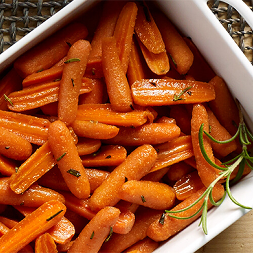 Carrots drizzled with garlic butter and honey, covered in herbs, served in a white tray on a wired table mat.