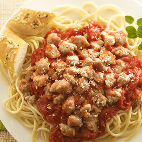 A hearty portion of spaghetti, turkey, and parmesan cheese, served with garlic bread, on a white plate, atop a green cloth.