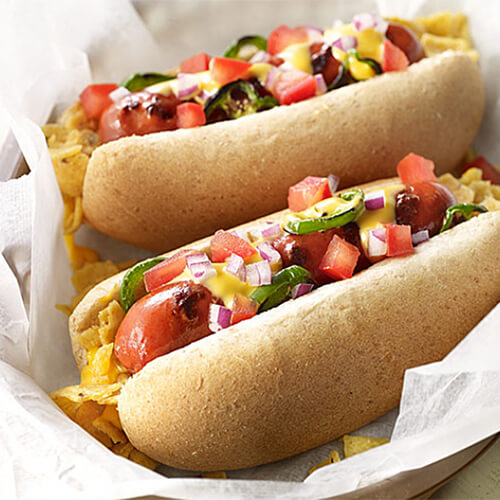 A simple dog with jalapeno peppers, corn chips, tomatoes and red onions, topped with gooey cheese sauce and served in parchment paper.