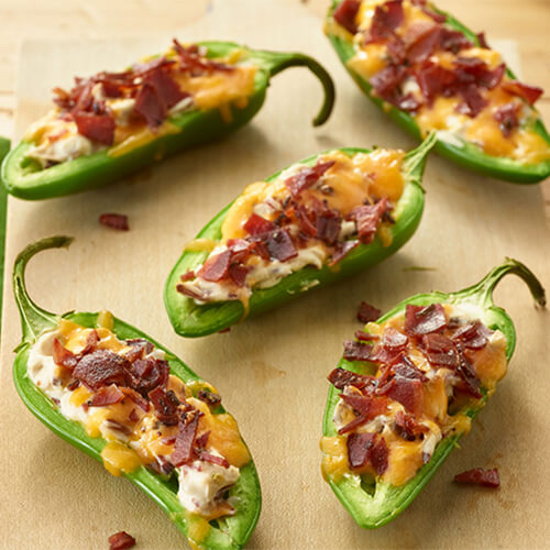 Five jalapeno turkey bacon poppers on a beige background.