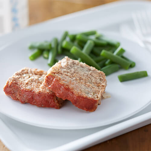 Lean ground turkey meatloaf loaded with flavorful ingredients like jalapeno and sweet red peppers, served on a white plate with a side of green beans.