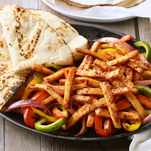 Grilled turkey strips with roasted green and red bell peppers with onions on a black plate with folded tortillas.