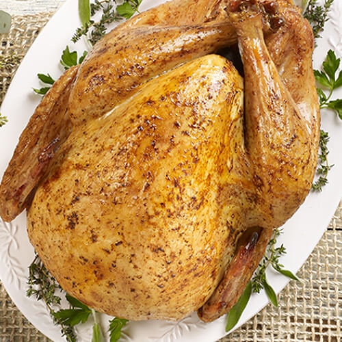 A delicious pre-seasoned turkey garnished with herbs on a white plate served with a side of savory gravy, on a wired table mat.