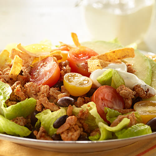 A hearty portion of savory ground turkey, fresh veggies and ranch dressing, served on a white plate atop a yellow cloth.