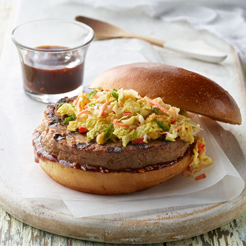 Korean barbeque turkey burger with a side of sauce on a marble plate.