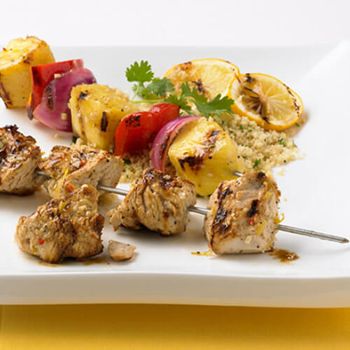 Chunks of turkey, charred pineapple, red pepper, and onions, on a metal skewer.